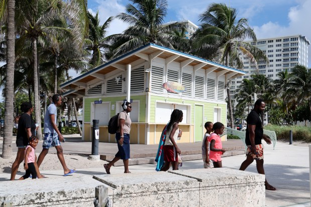 A family walks past Sandbar Snacks on Pompano Beach, Thursday, August 1, 2024. (Carline Jean/South Florida Sun Sentinel)