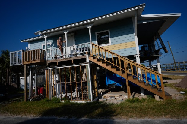 Jim Johnson sits atop the railing at the entrance to his stilted home in Horseshoe Beach, Fla., Wednesday, May 8, 2024. While Hurricane Idalia storm surge damaged the stairs and downstairs utility room and sheared off part of the waterfront balcony sheared off, the Johnsons were relieved that the damage wasn't great enough for FEMA to require them to raise the house on higher stilts to meet current code requirements. (AP Photo/Rebecca Blackwell)